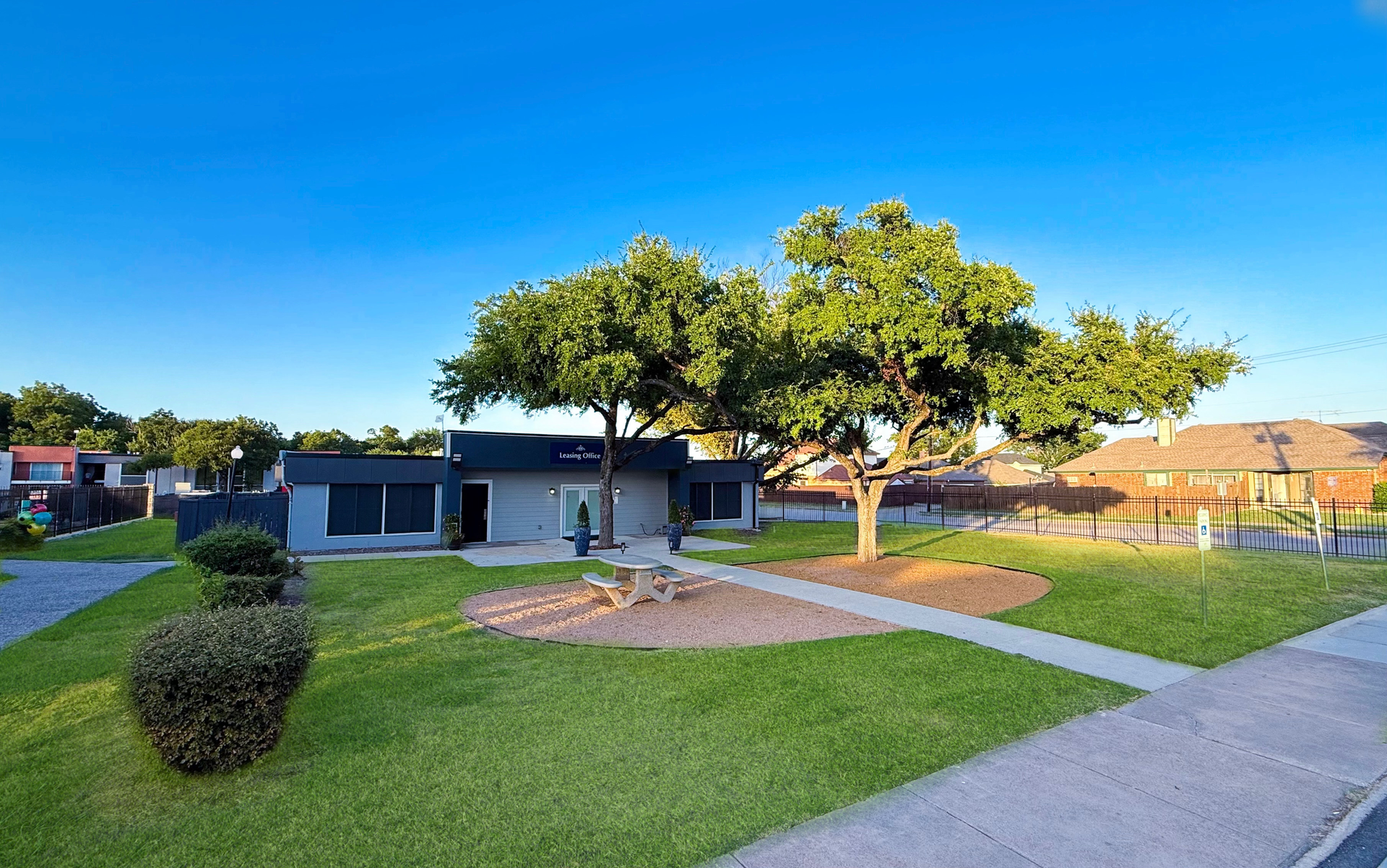 A small modern building with trees in a grassy park under a clear blue sky.