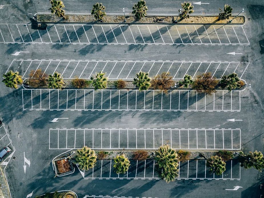 Overhead view of an empty parking lot with white painted parking spaces, rows of trees.