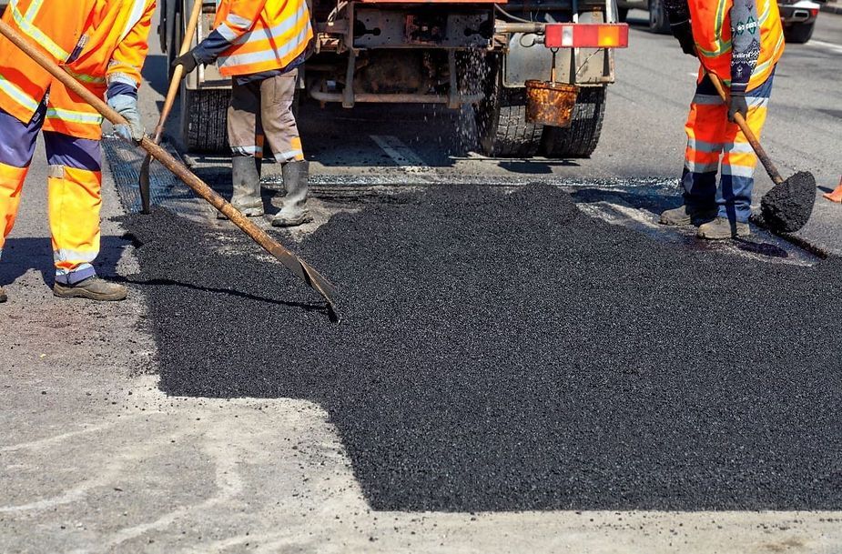 Road workers in orange vests and pants paving a section of asphalt road.