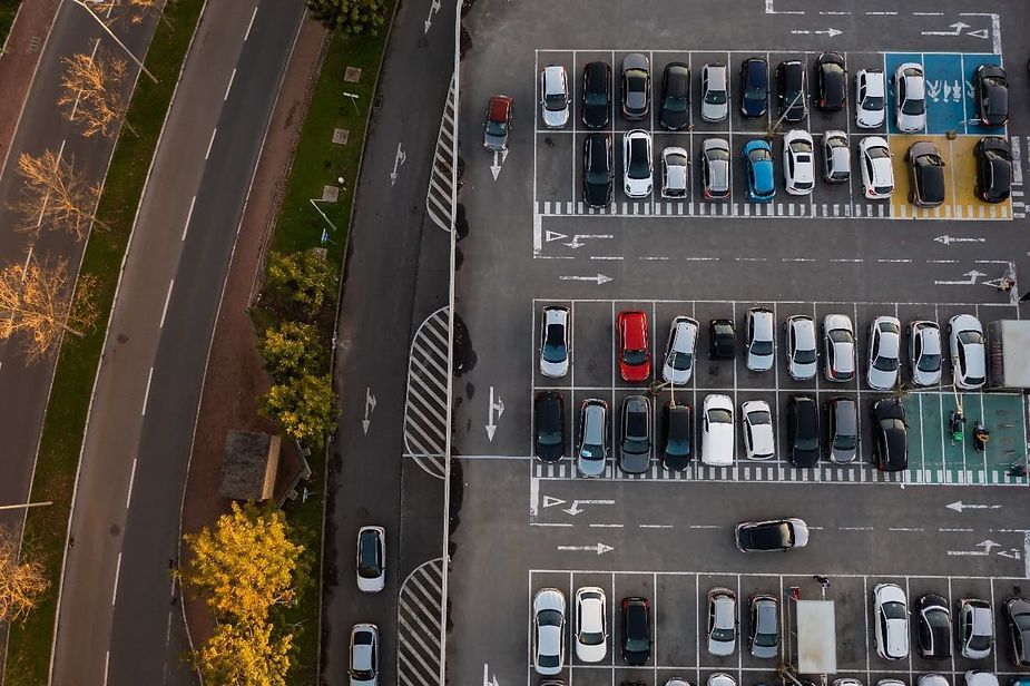 Aerial view of a parking lot with numerous parked cars, a road, and green space.