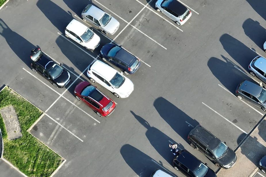 Cars parked in an outdoor parking lot, viewed from above, on a sunny day.