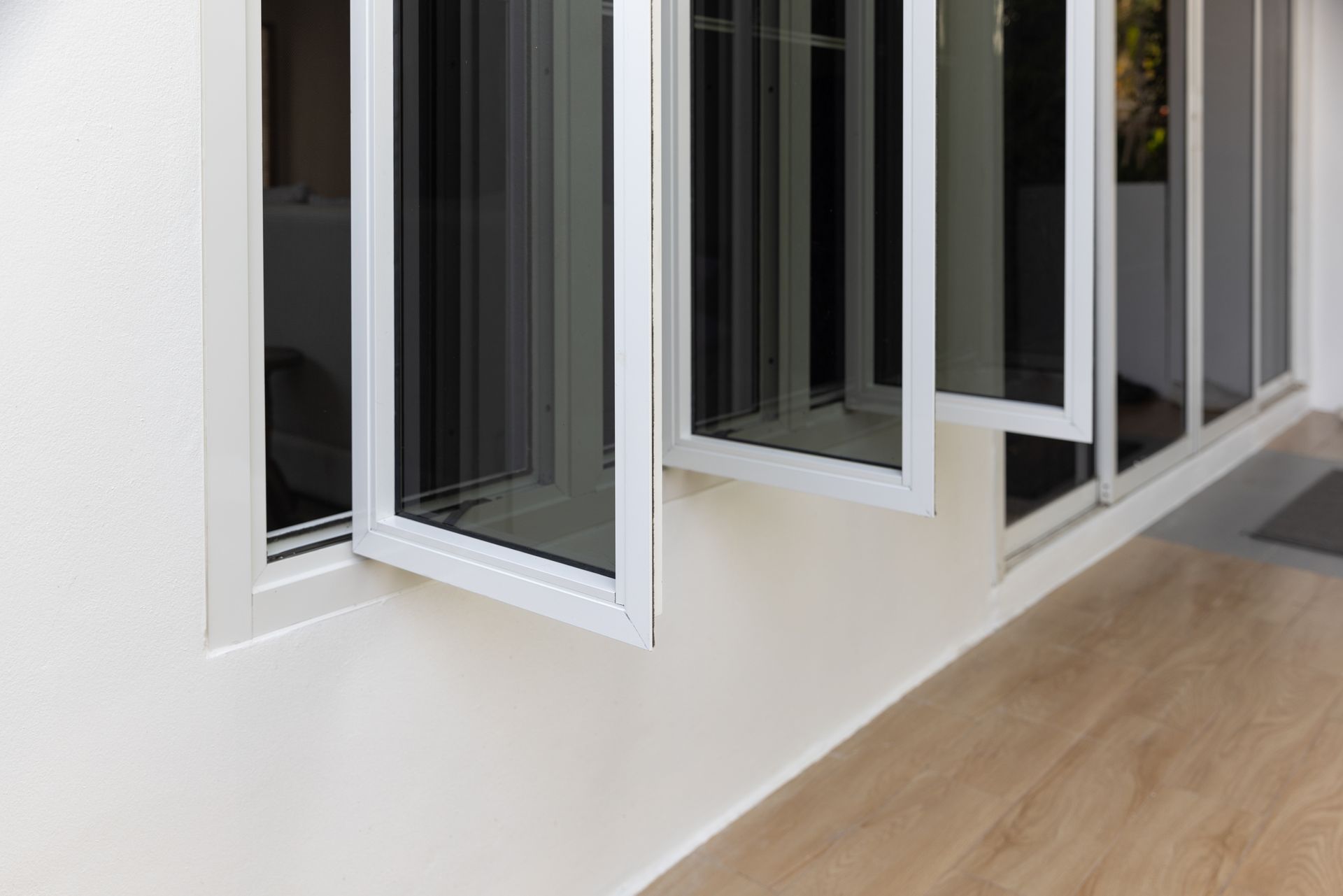 White framed windows are partially open, set in a white wall above a wood floor.