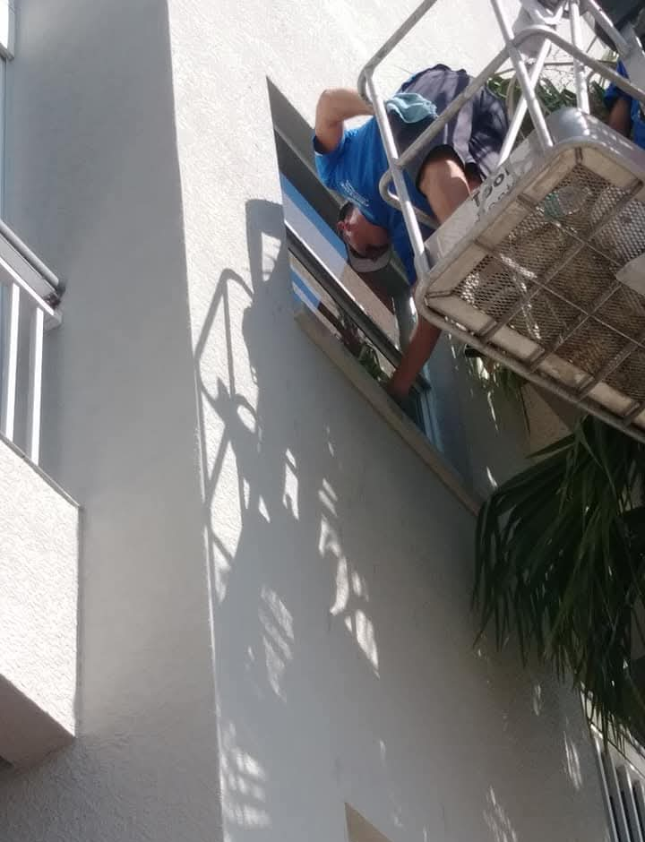 Person in a lift cleaning a window on a white building exterior.