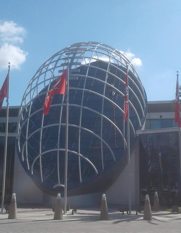 Large spherical metal structure resembling a globe in front of a building with red flags.