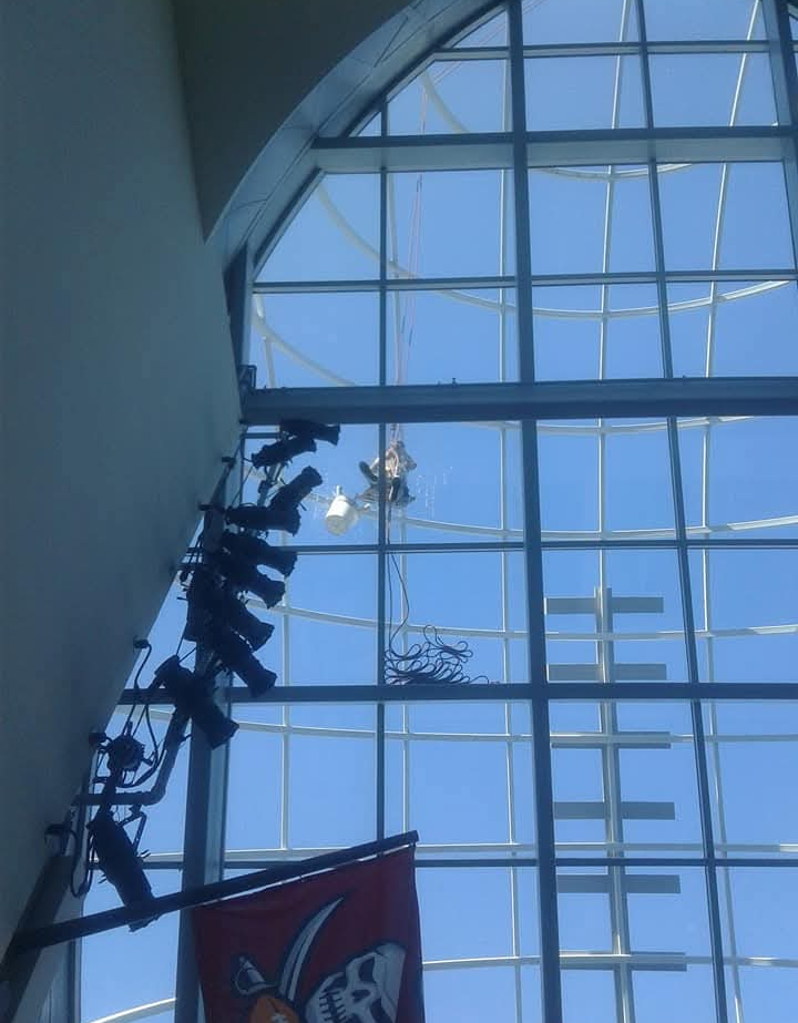 Window cleaner suspended by ropes, cleaning a large window with blue sky.