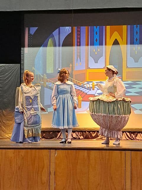 Three girls in blue dresses are standing on a stage talking to each other.