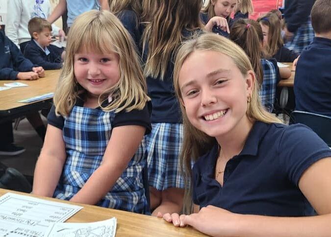 Two young girls are sitting at a table smiling for the camera.