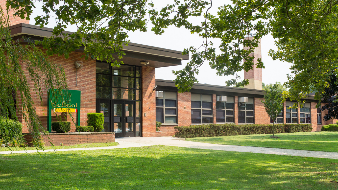 Modern building with glass front entrance, greenery, and sunlight.