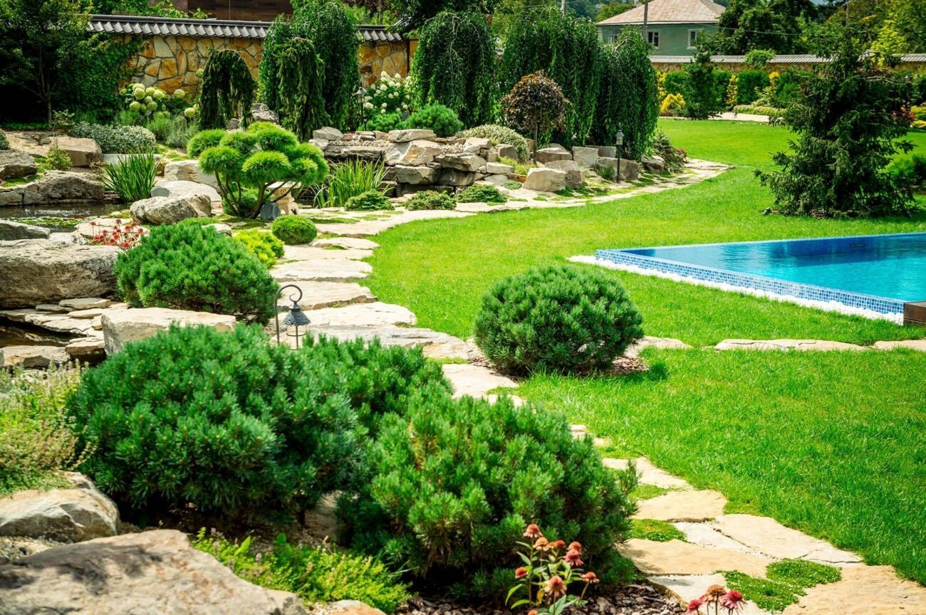 Green lawn bordered by a beige concrete edge, leading to a rock garden with bushes and gravel.