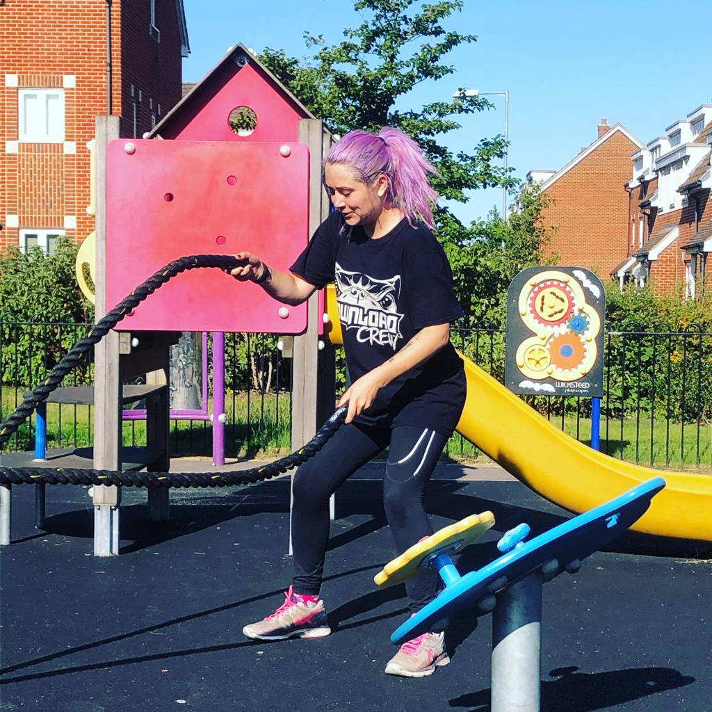 A woman with pink hair is playing with a rope in a playground