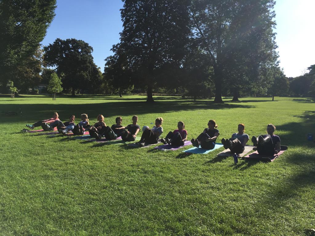 A group of people are sitting on yoga mats in a park.