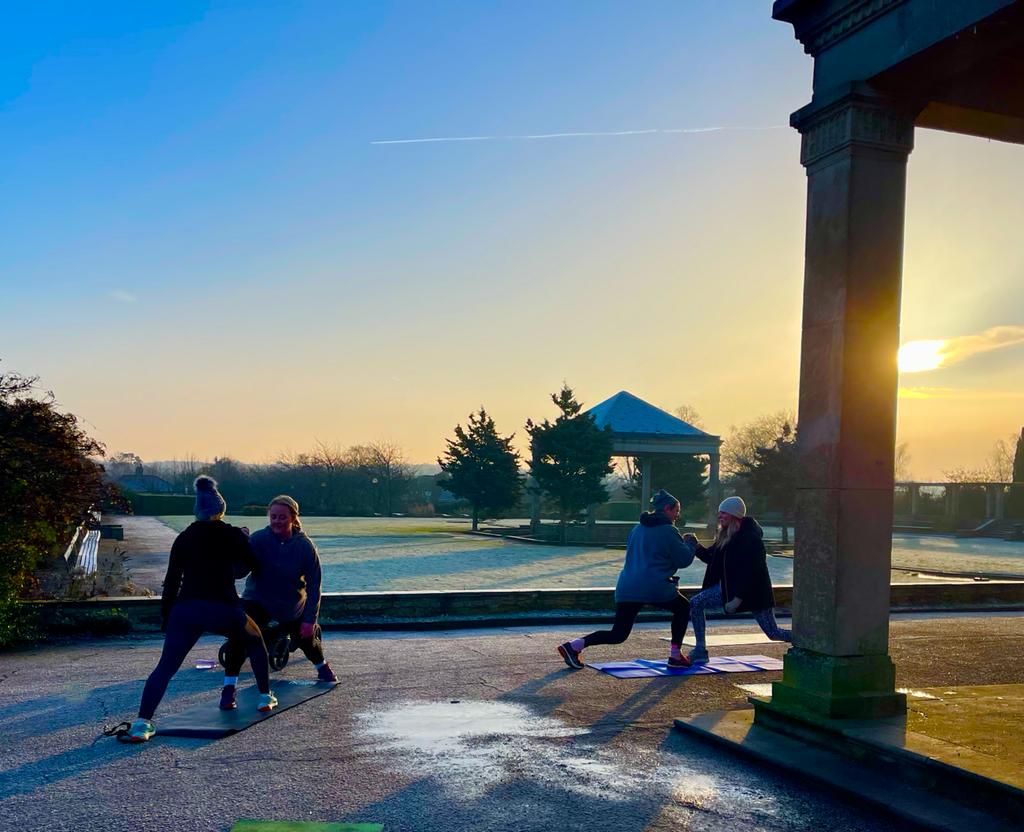 A group of people are practicing yoga in a park at sunset.