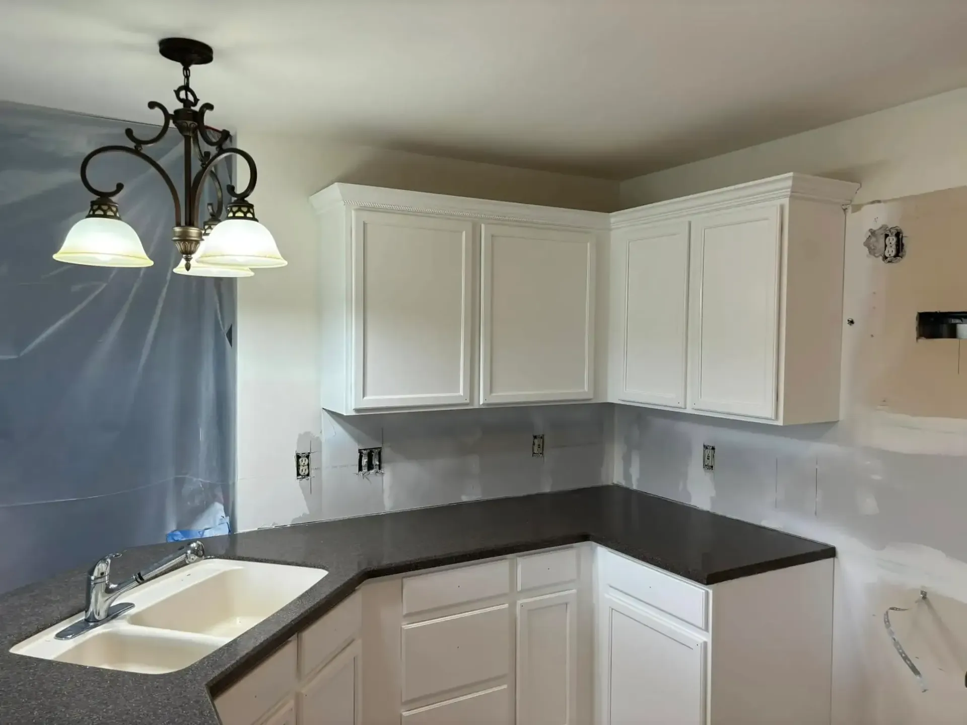 White kitchen cabinets with dark countertop, sink, and chandelier.