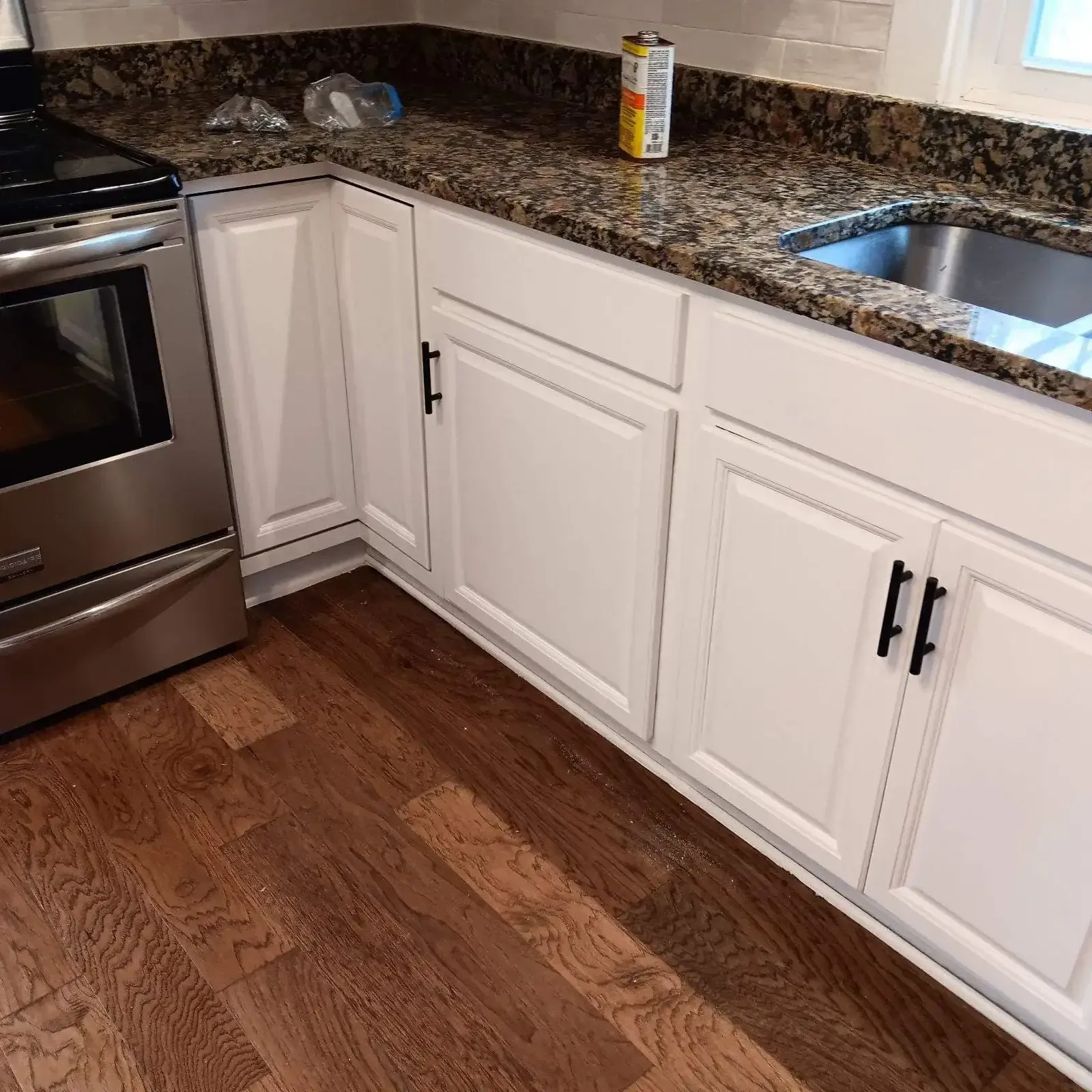 White kitchen cabinets with black handles, granite countertop, stainless steel appliances, and wood floor.