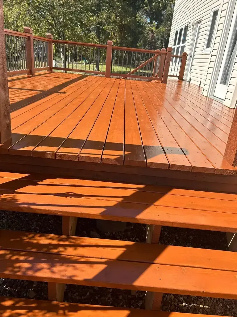 Newly stained wooden deck with steps, railing, and a house in the background; sunlight casts shadows. Newly stained wooden deck with steps, railing, and a house in the background; sunlight casts shadows.