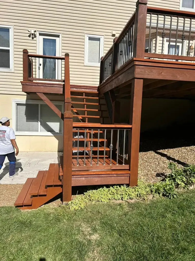 Brown wooden deck with stairs attached to a beige house, with a person standing nearby. Brown wooden deck with stairs attached to a beige house, with a person standing nearby.