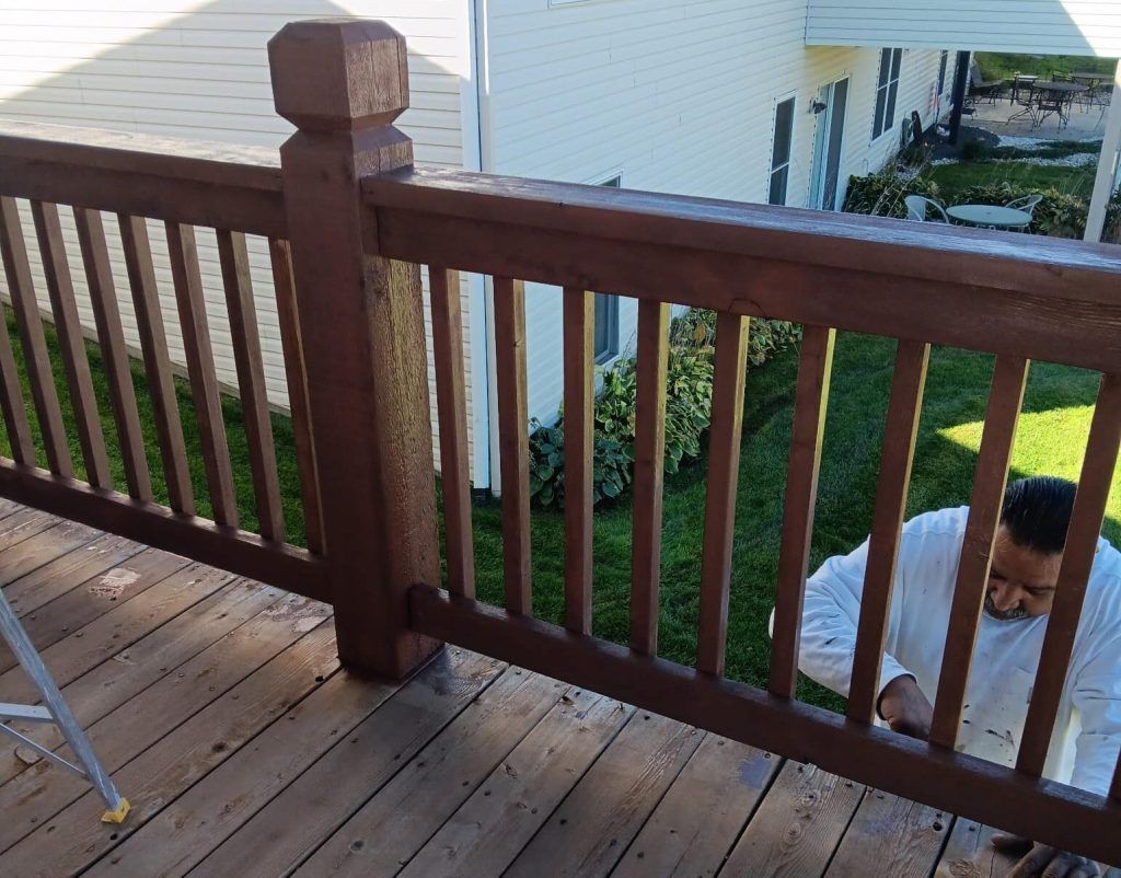 Person painting brown deck railing on a wooden deck. Person painting brown deck railing on a wooden deck.