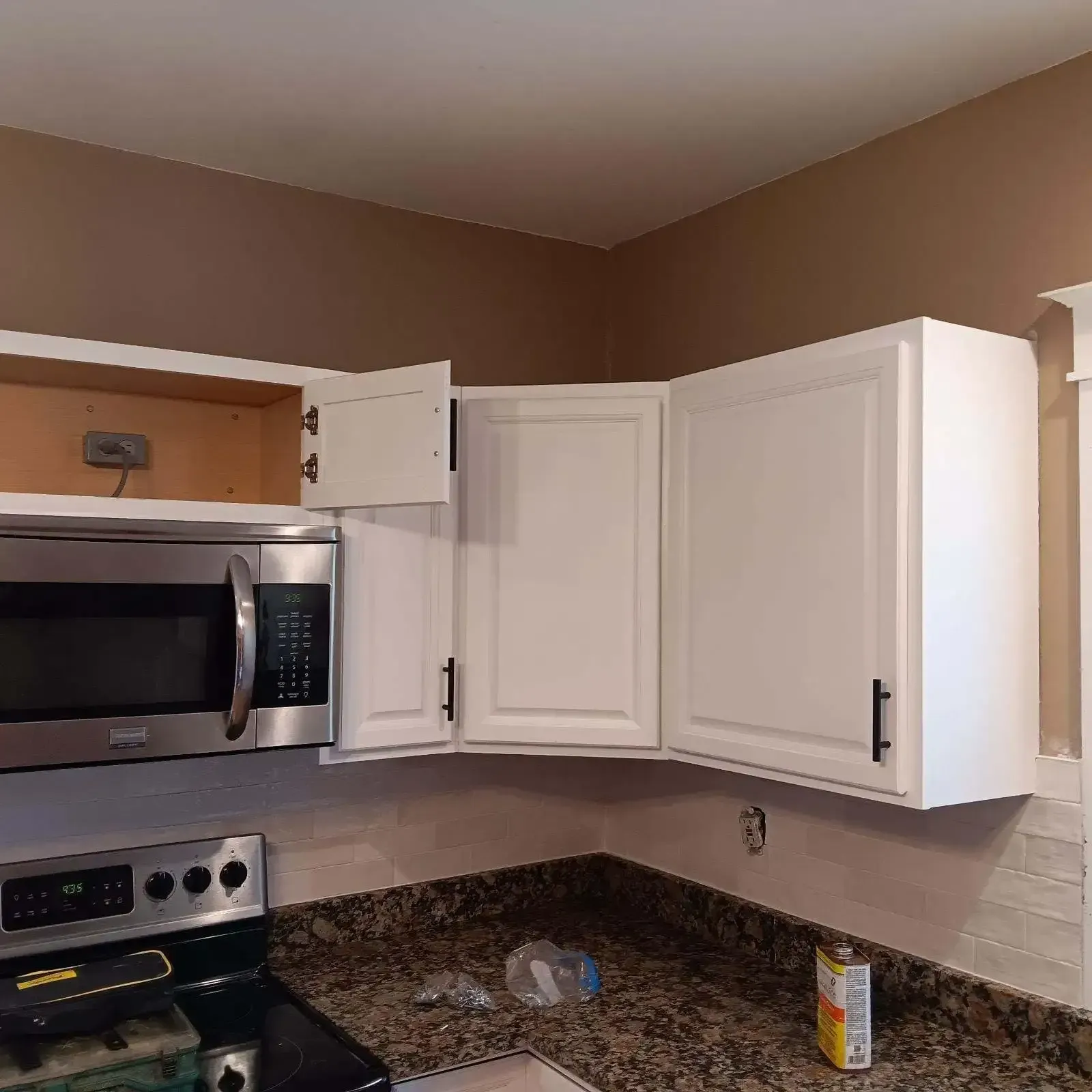 White kitchen cabinets, microwave, and stove installed, countertop, with one cabinet door open.