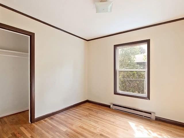 Empty room with tan walls, brown trim, hardwood floor, window, and closet.