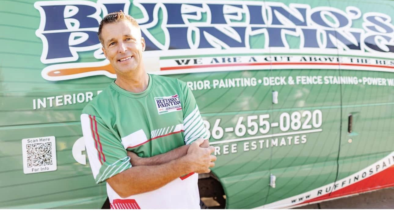 Man with arms crossed smiles in front of green and white Man with arms crossed smiles in front of green and white