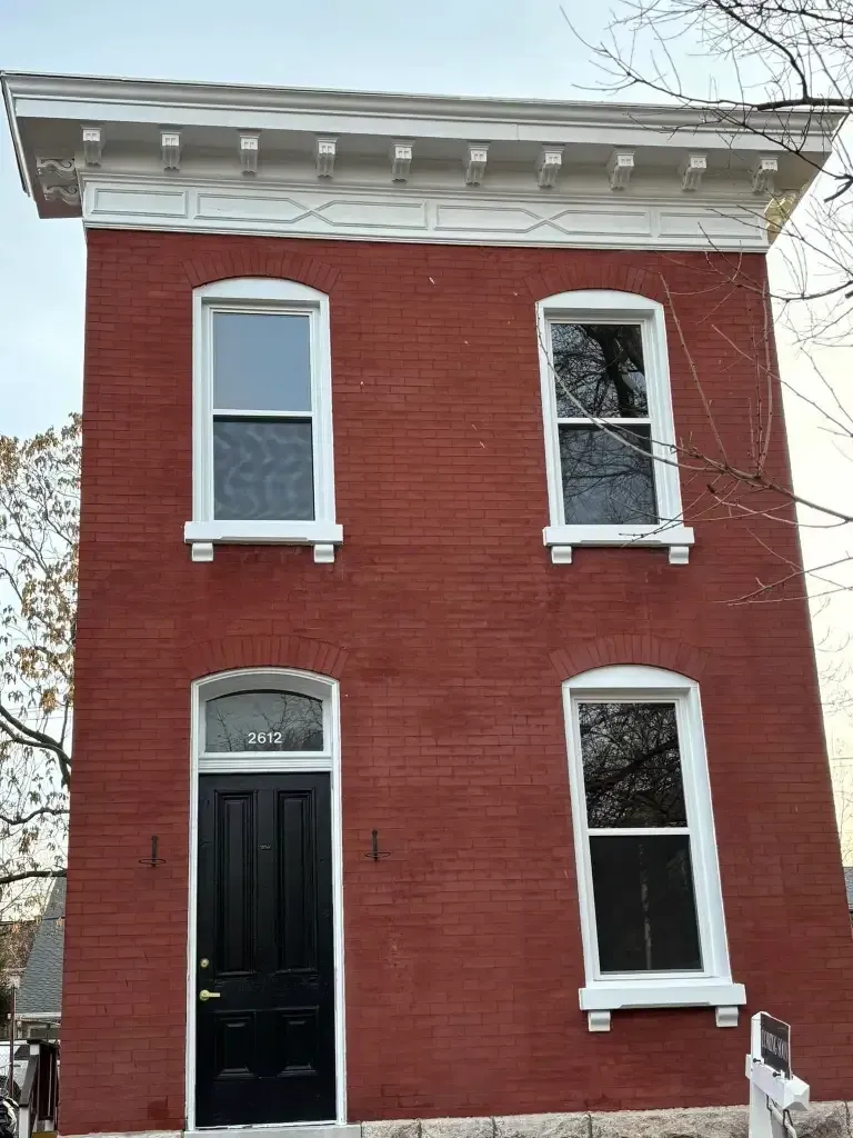 Red brick two-story house with white trim around windows and decorative cornice. Black front door.