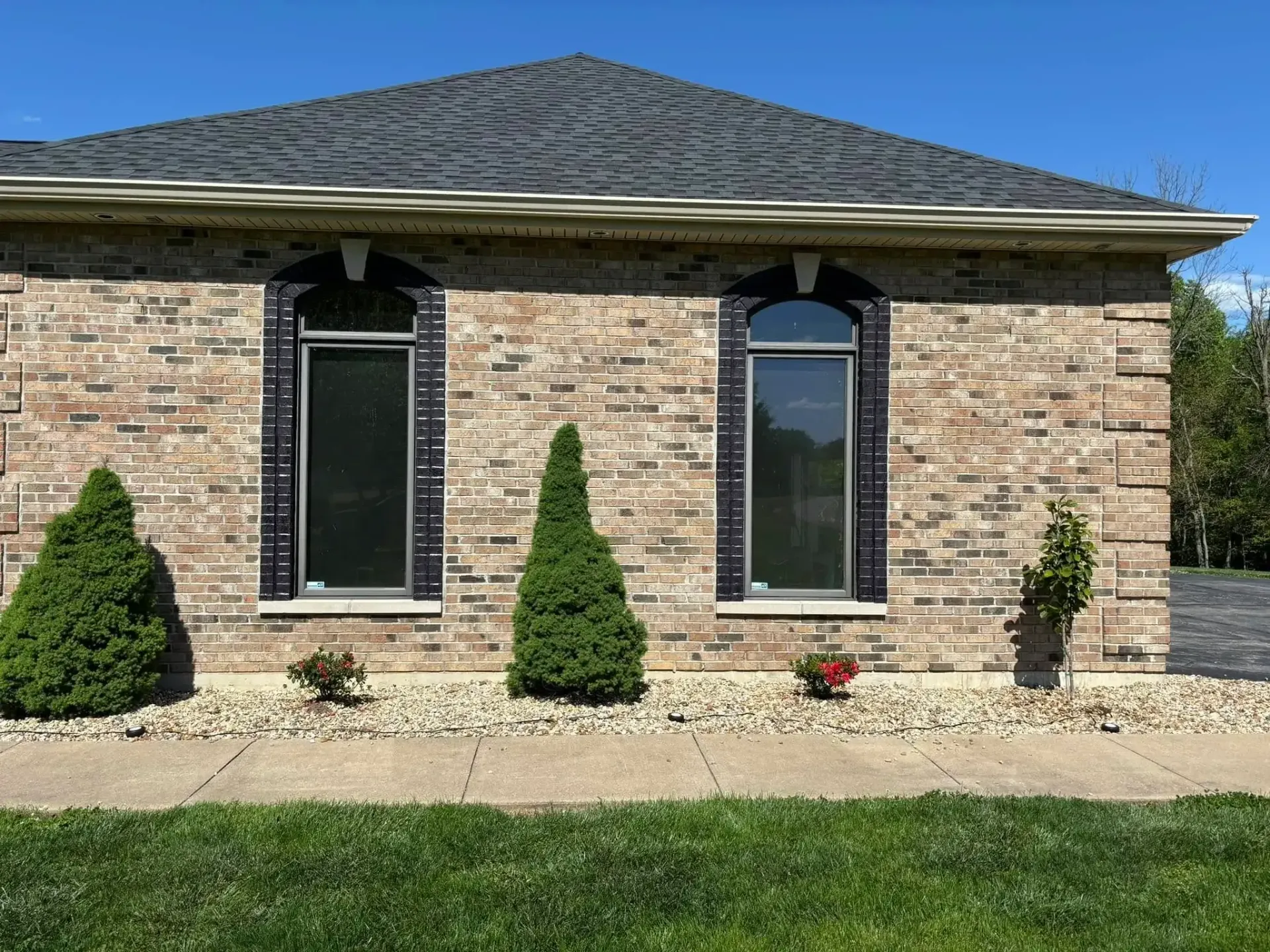 Brick house with two arched windows, black shutters, and landscaping under a blue sky.