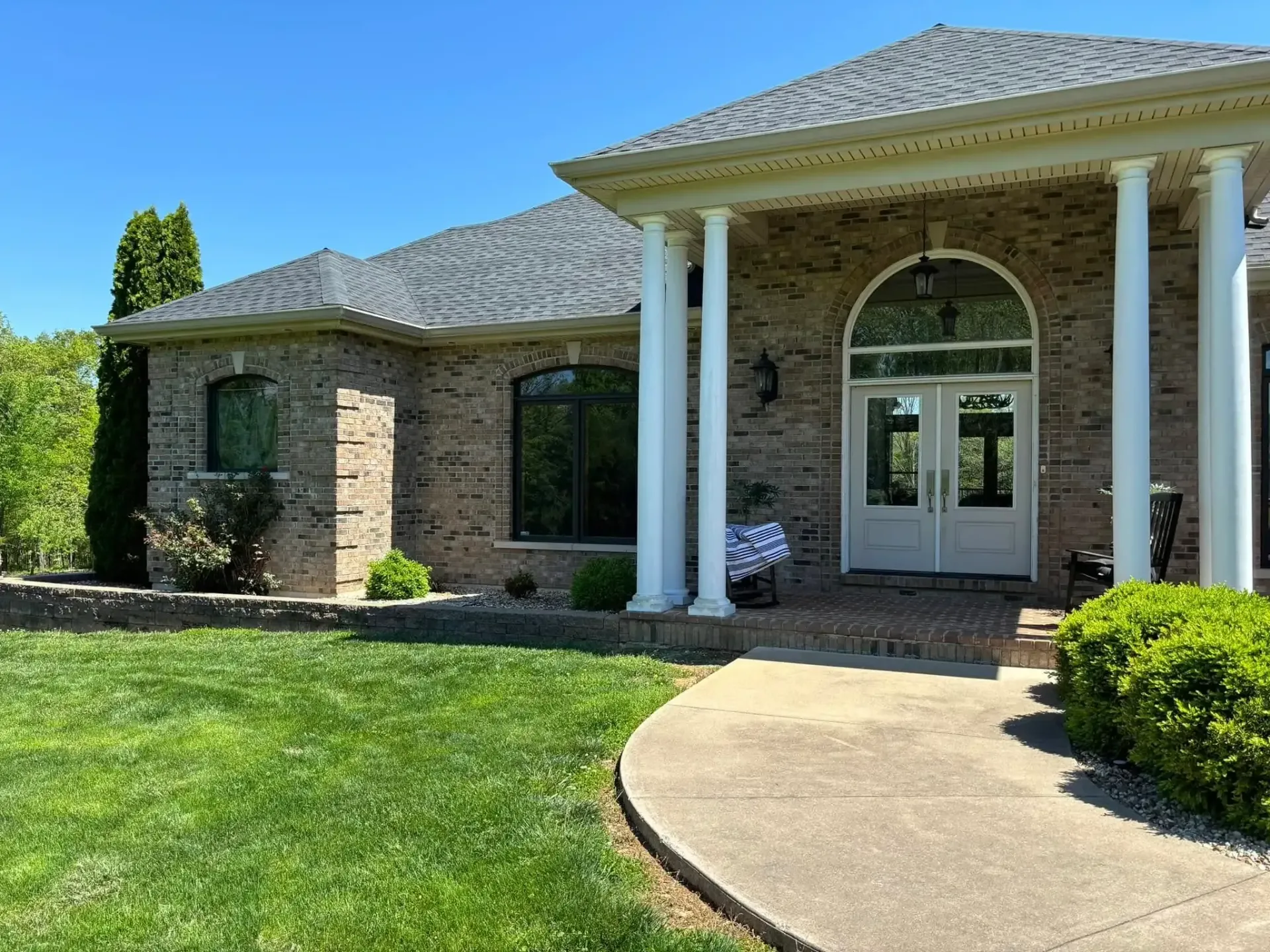 Brick house with white columns, arched doorway, and a curved walkway.