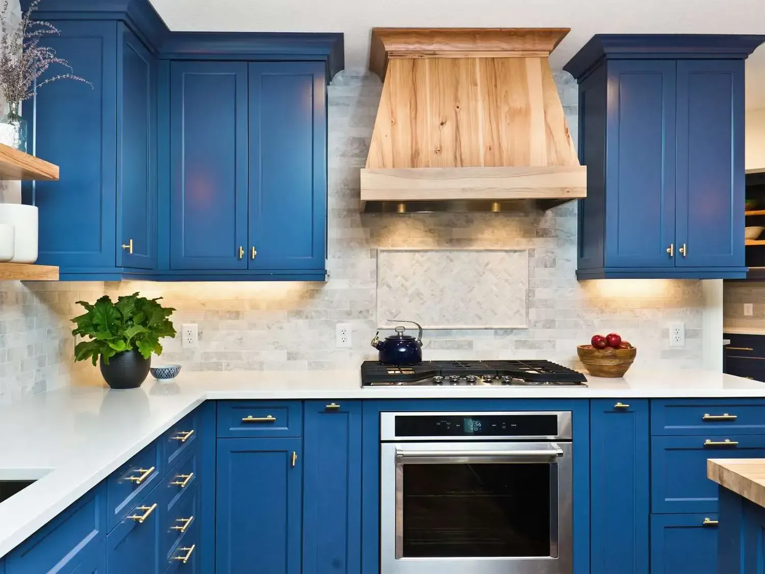 Blue kitchen cabinets with white countertops, a wooden range hood, and stainless steel oven.