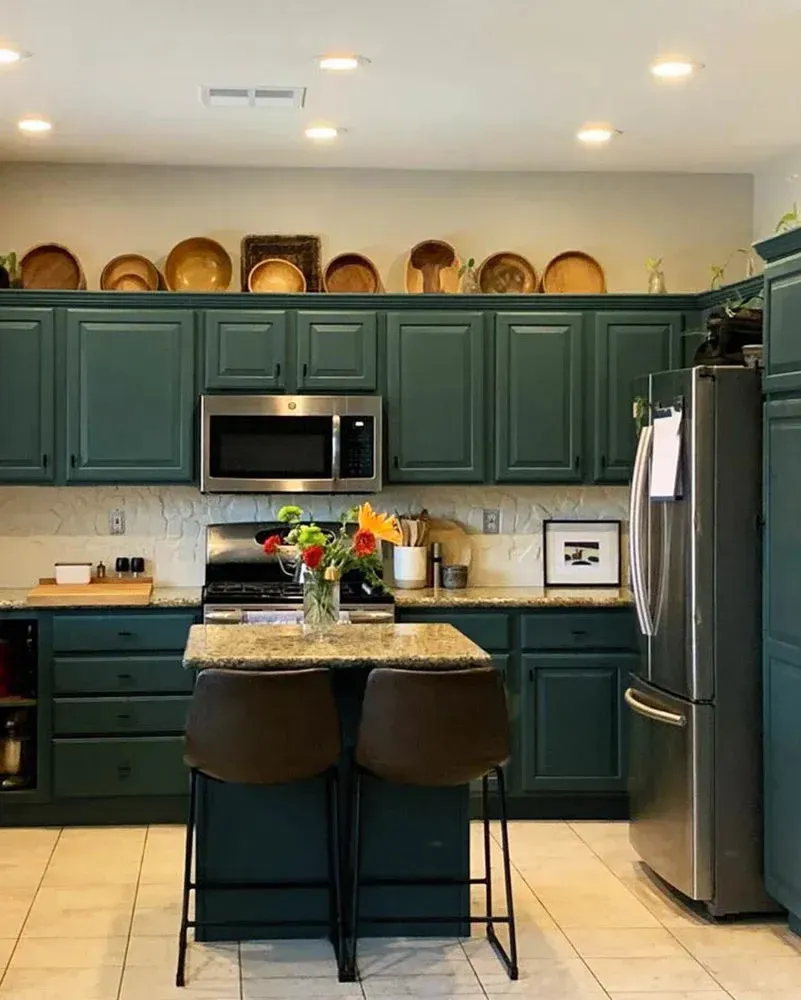 Green kitchen with island and stainless steel appliances. Dishes line the top cabinets.