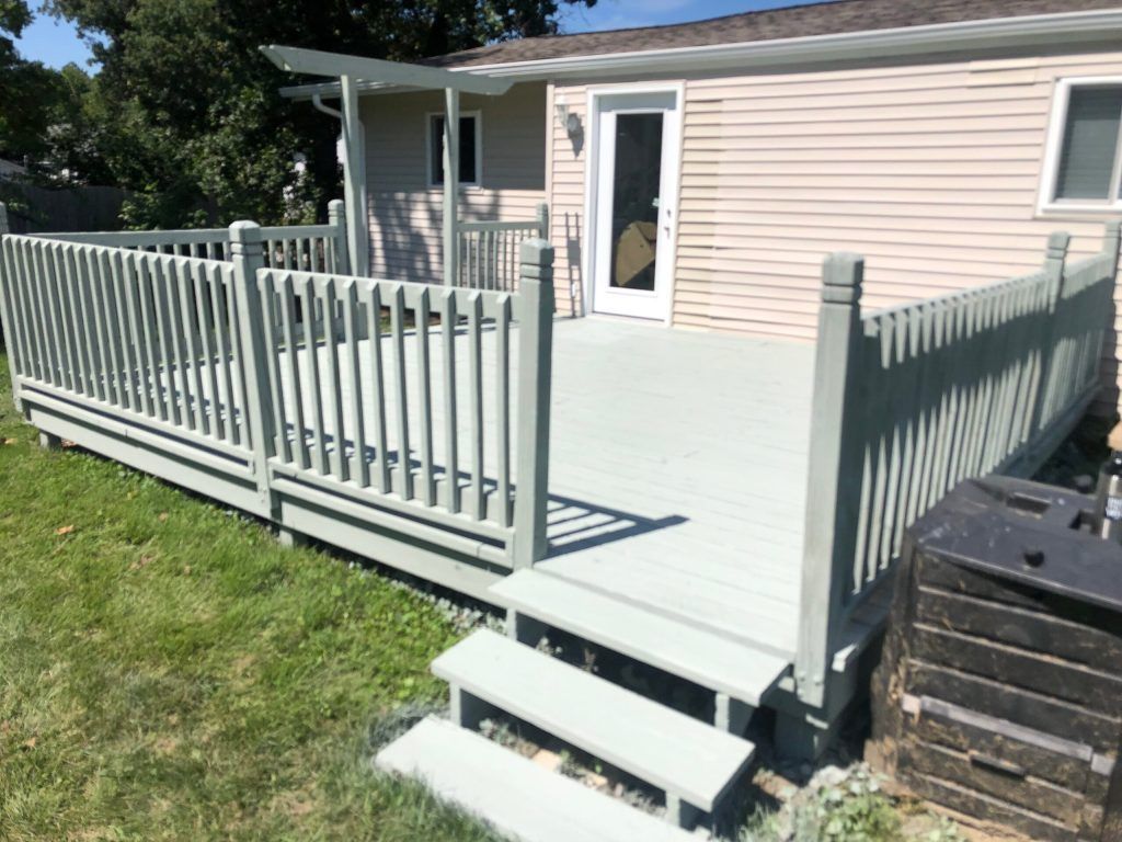 Light green deck with steps in a backyard, beside a light beige house.