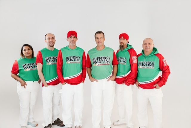 Team of painters in green and red shirts and white pants, standing in front of a white background.