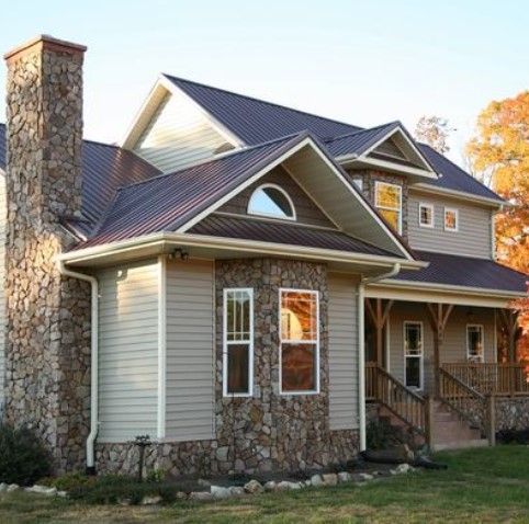 Two-story house with stone accents, tan siding, brown roof, and chimney. Sunlight reflects in windows.