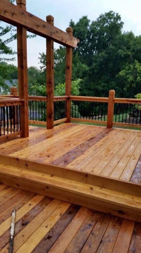 Wooden deck with arbor, railings, and steps. Wet boards with dark metal and green trees in background. Wooden deck with arbor, railings, and steps. Wet boards with dark metal and green trees in background.