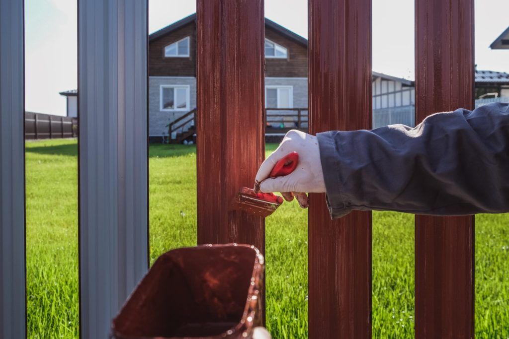 Person in gloves painting a red metal fence outdoors. Person in gloves painting a red metal fence outdoors.