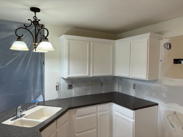 White kitchen cabinets with black countertop; a sink and a chandelier are visible.