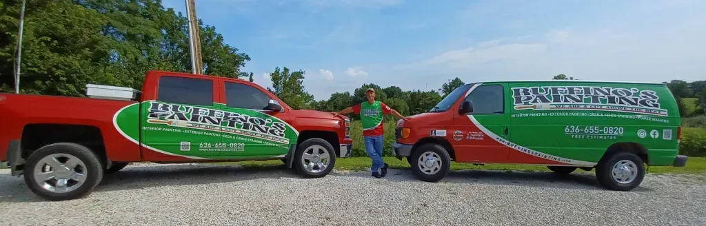 A person stands between a red pickup truck and a green van, both with business logos on a gravel road. A person stands between a red pickup truck and a green van, both with business logos on a gravel road.
