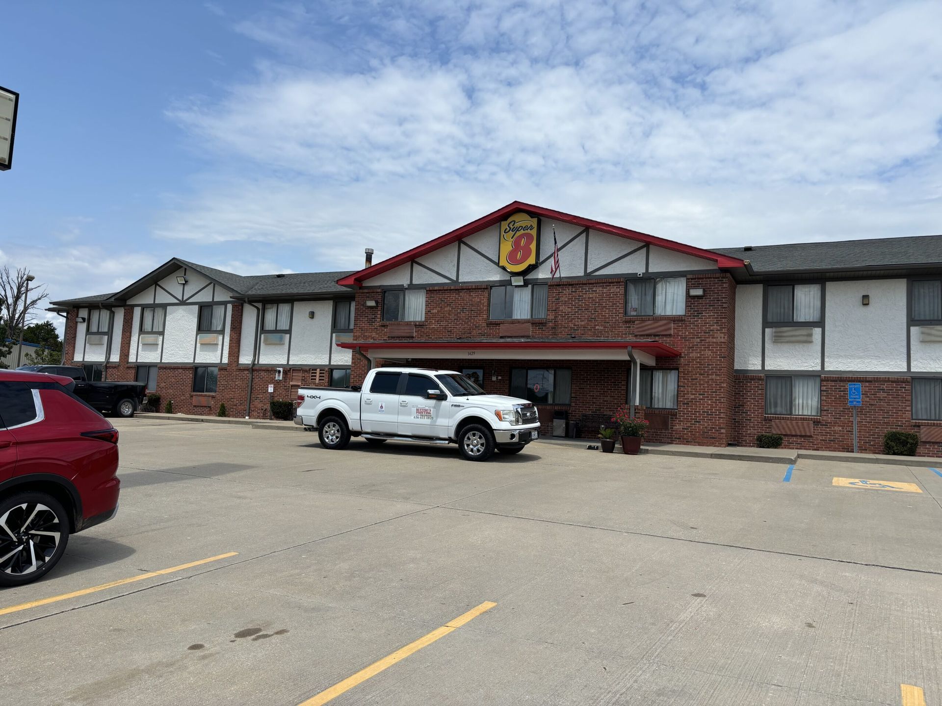 A person stands between a red pickup truck and a green van, both with business logos on a gravel road.