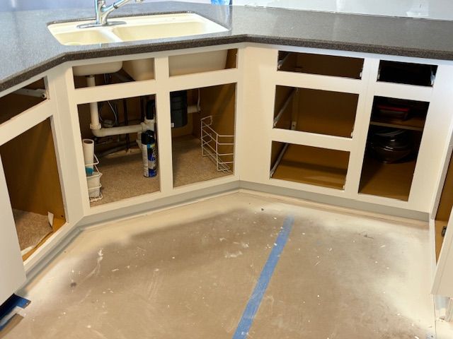 Kitchen cabinets being installed, with unfinished white frames and empty openings. Gray countertops and a sink are visible.