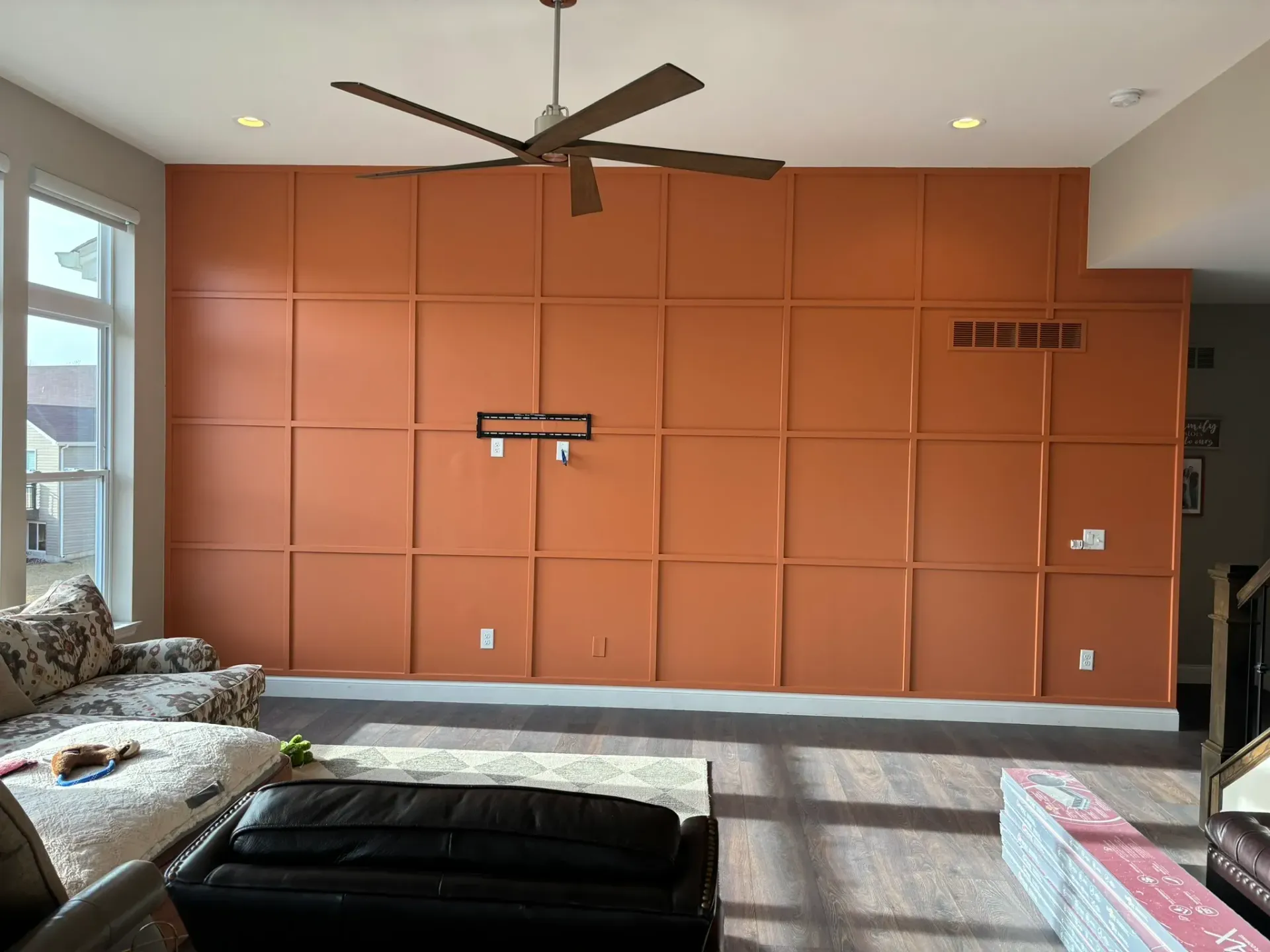 Orange paneled wall with a ceiling fan, a sofa, and hardwood floors.