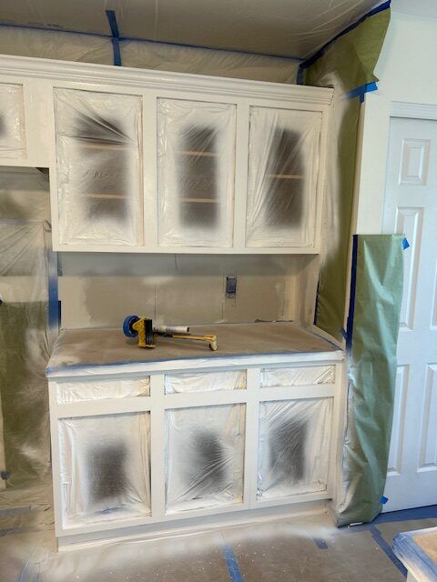 Kitchen cabinets covered in plastic for painting; white paint visible.