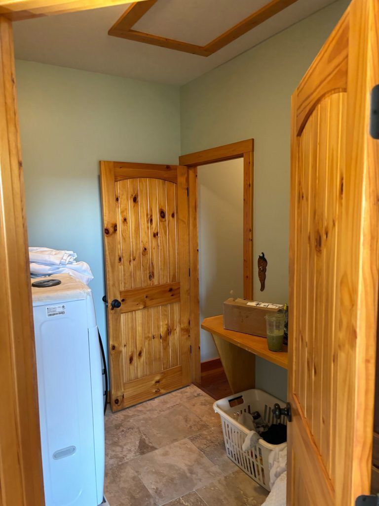 Laundry room with light blue walls, wood doors, white washer, and a wooden shelf.