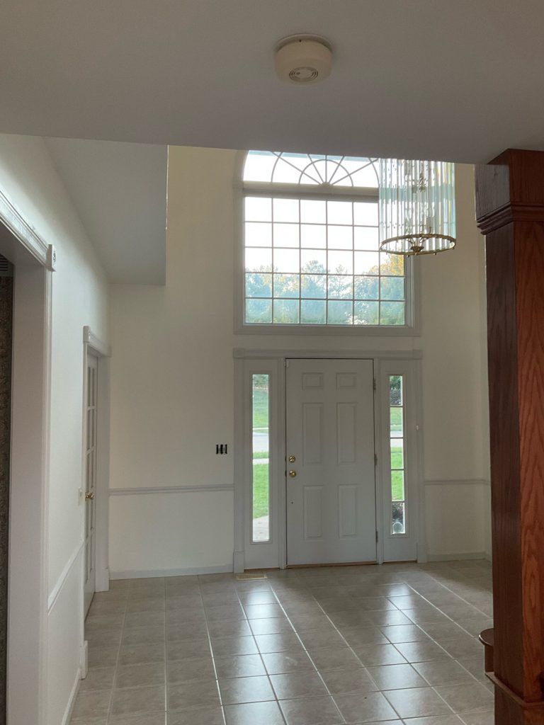 Spacious entryway with tall door and window, chandelier, neutral walls, tile floor.