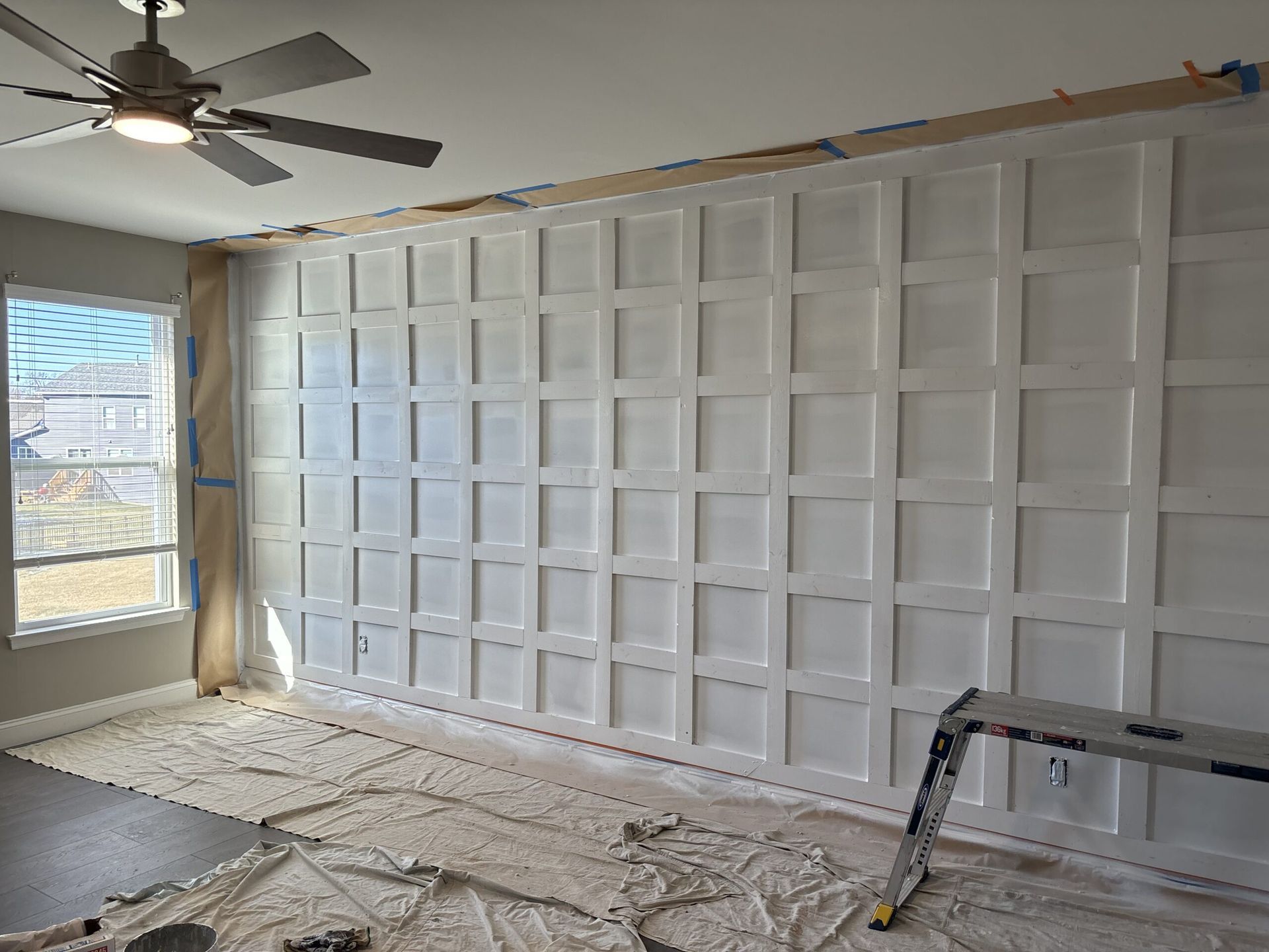 White grid panel wall in a room, with a window and a ceiling fan.