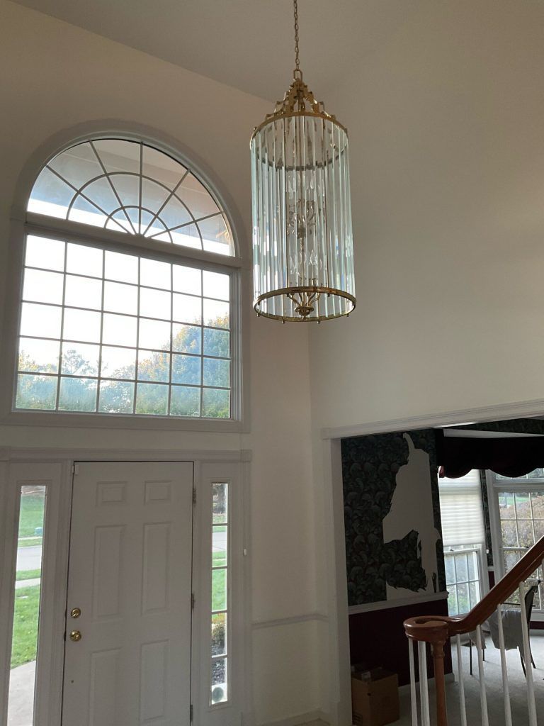 Entryway with arched window, chandelier, and front door. White walls, gold chandelier, and view of trees outside.