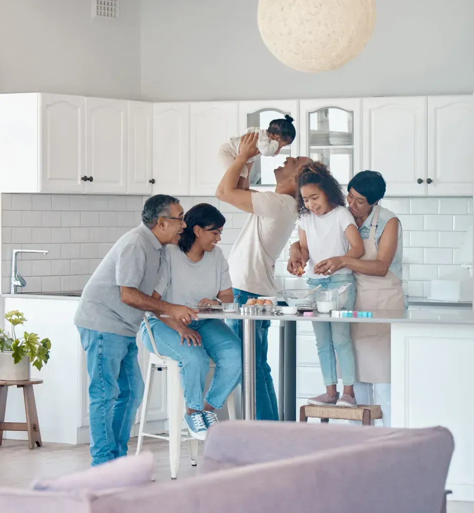 Family baking together in a bright kitchen; parents and grandparents with children, one lifted up. Family baking together in a bright kitchen; parents and grandparents with children, one lifted up.