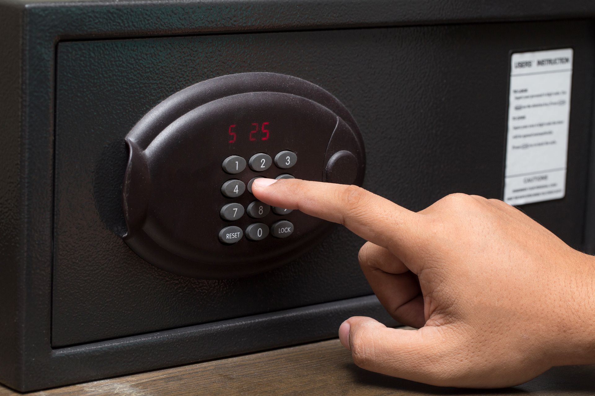 Close-up of a hand pressing the buttons of a black, electronic safe. Close-up of a hand pressing the buttons of a black, electronic safe.