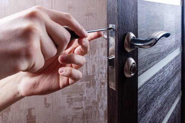Carpenter installs a door lock, showcasing locksmith services, adjusting screws precisely.