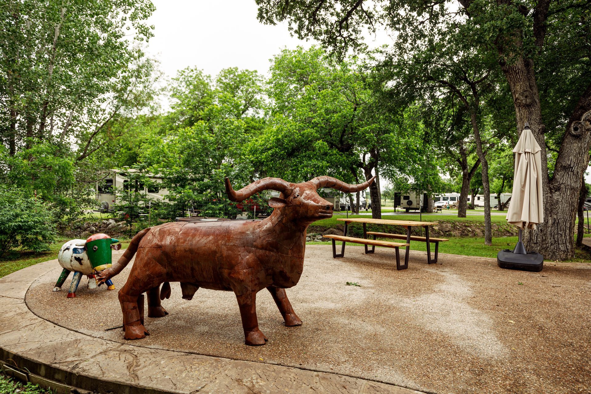 A statue of a goat is standing in a park next to a picnic table.