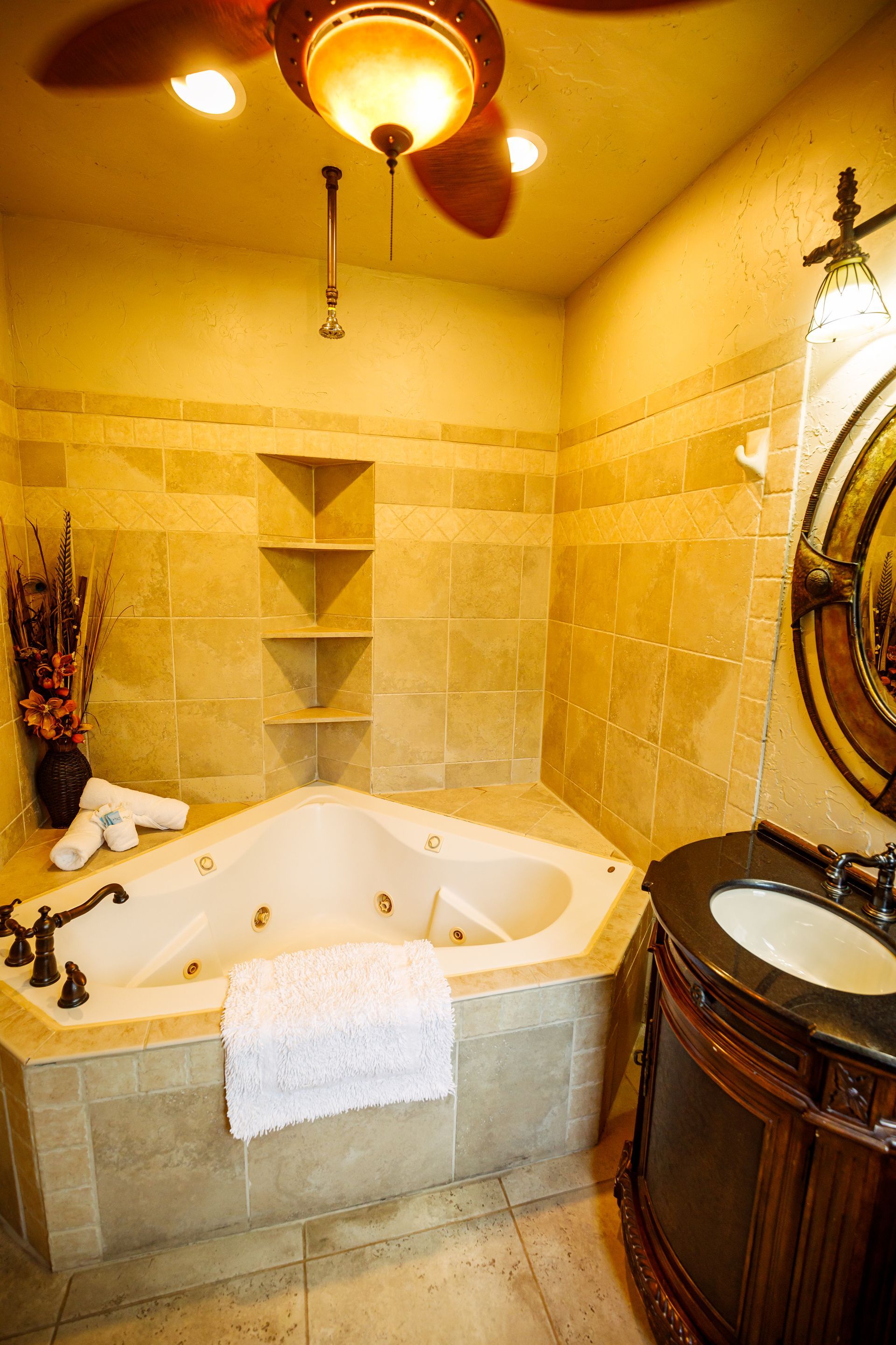 A bathroom with a jacuzzi tub , sink , mirror and ceiling fan.