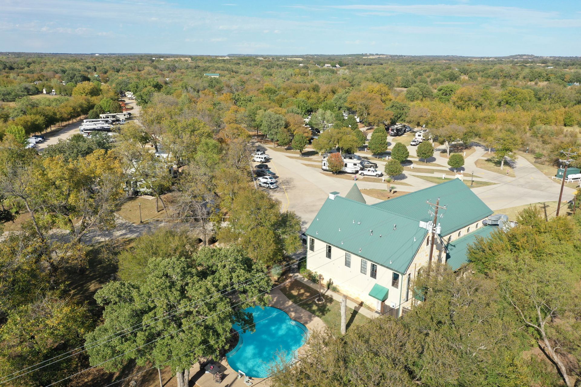 An aerial view of a house with a green roof and a pool surrounded by trees.